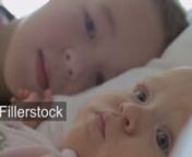 A closeup of two kids&#39; faces. A six months old baby girl is lying on a white pillow. Her elder brother is lying right behind her. He is rising a head and kissing a baby on her soft cheeknLicense this clip: https://fillerstock.com/video/13738