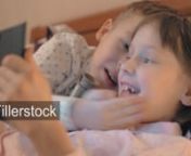 Children lying in bed and playing game on tablet PC. Lovely boy and girl kissing each other by turnnLicense this clip: https://fillerstock.com/video/11983