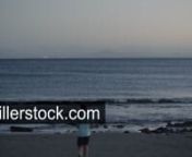 Boy running up the ocean and throwing stones into the water. Evening scene on black sand beach of Lanzarote, Canary IslandsnLicense this clip: https://www.shutterstock.com/ru/video/clip-1061699086-boy-running-ocean-throwing-stones-into-water